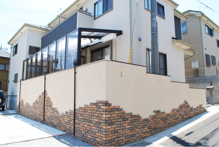 傾斜地に建てられた建売住宅のリガーデンです。汚れてしまったコンクリートの擁壁を、レンガと塗装で洋風にアレンジしました。壁の下段だけレンガを貼る事で、壁の不安定感を無くし、ずっしりとした印象になりました。ランダムに貼られたレンガも動きがあり、古城のような雰囲気を出しています。 《ガーデンリフォーム工事写真集》-津久井様邸-01