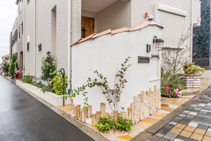 角地に位置するご新築にお住いの金子様。ご新居を囲う2面を石材、白い塗り壁、植栽で彩り、安らぎと統一感を併せ持ったセミクローズエクステリアをデザインしました。形状の違う暖色系の自然石をアプローチやデザインウォールに組み込み、華やかさと温かみが感じられますね。